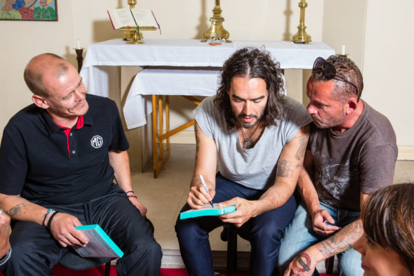 Russell Brand signs his copies of new book for Big Issue vendors Steve and Peter, photographed by Louise Haywood-Schiefer for The Big Issue at St John's Church in London