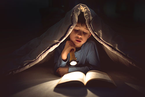 Boy reading a book under the bed covers