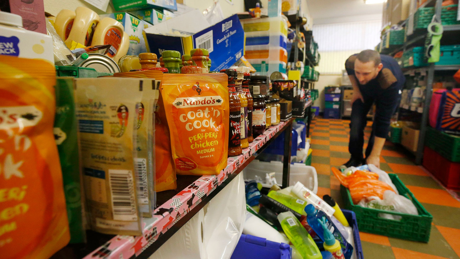 Packages of food are lined along shelves and on the floor in a food bank
