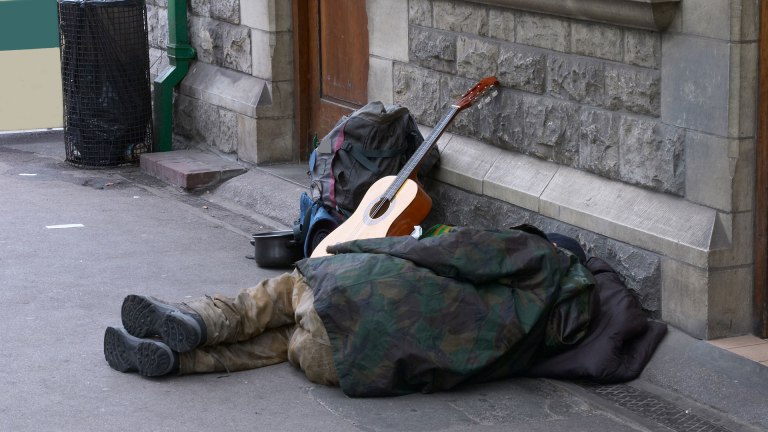 a person lies on the pavement facing away from the camera, with a guitar propped up beside them