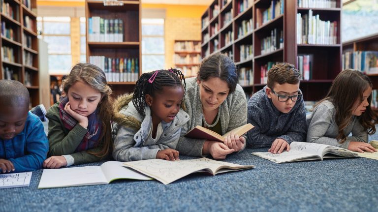 group of elementary school kids and their teacher lying down while working in the library