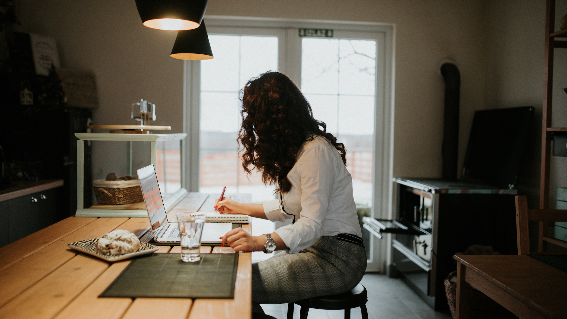 a woman works at a table with a laptop and a glass of water