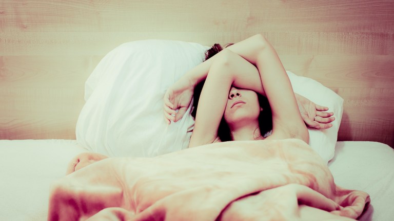 A woman lies in bed with her arms covering her face