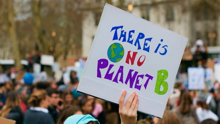 In a crowd of people outdoors, a hand holds up a placard that reads 