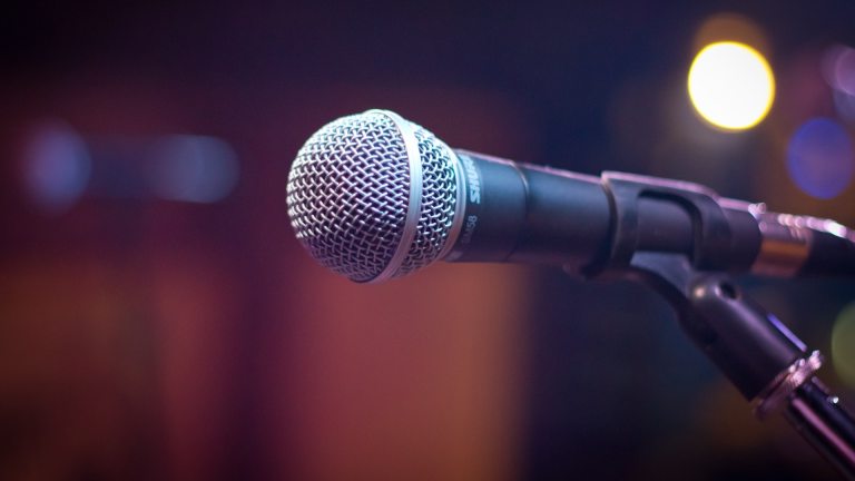 A microphone stands in the foreground with a blurry background