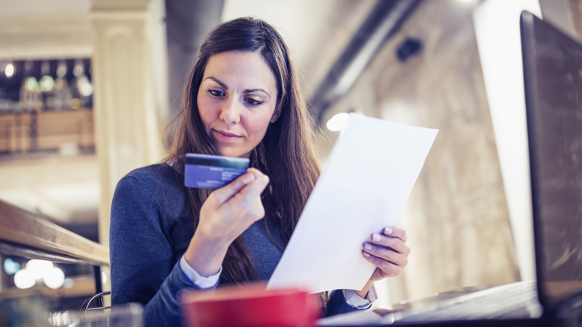 A woman checks her credit score holding a bank card and a sheet of paper
