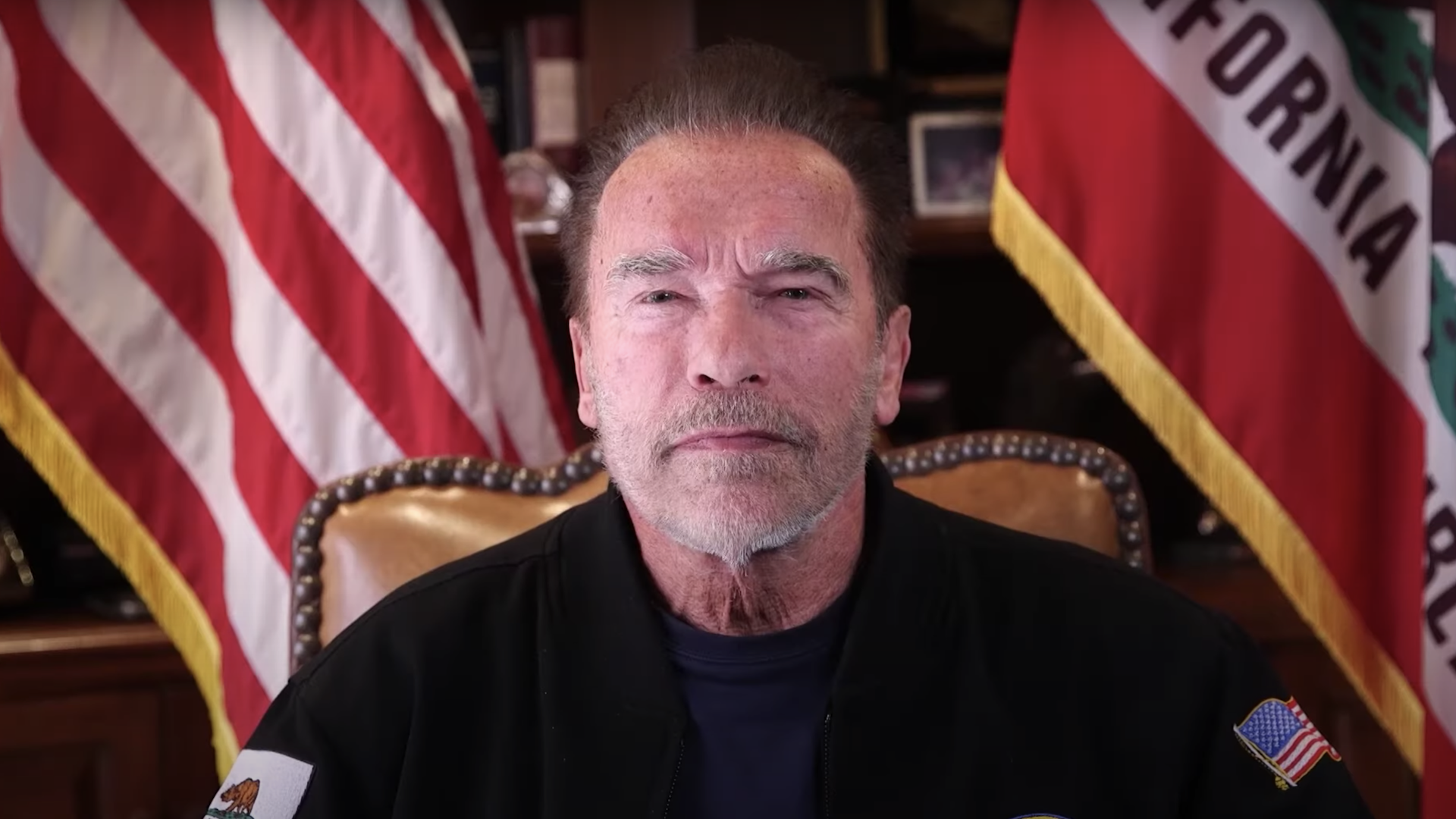 Arnold Schwarzenegger giving a speech in front of an American and Californian flag