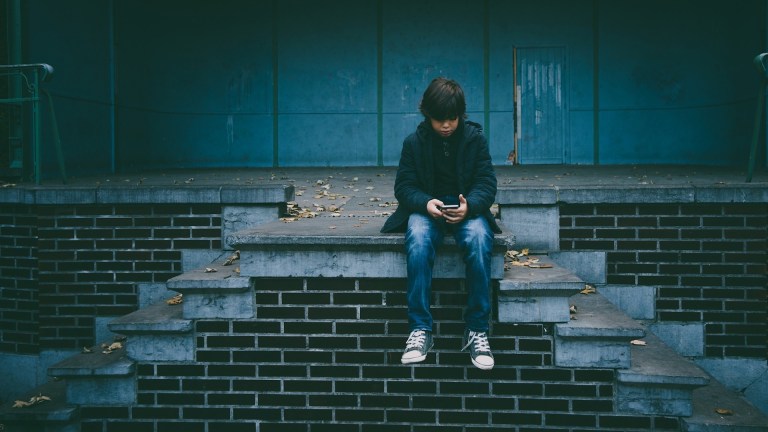 A boy sits on steps alone looking at his mobile phone. The Children's Commissioner said ministers must step up to improve children's mental health