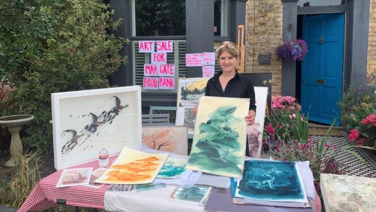 Artist Twinkle Troughton displays some of her art in front of a sign that says 