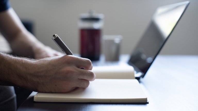 Man makes notes on a coffee table during work from home. Coffee in background.