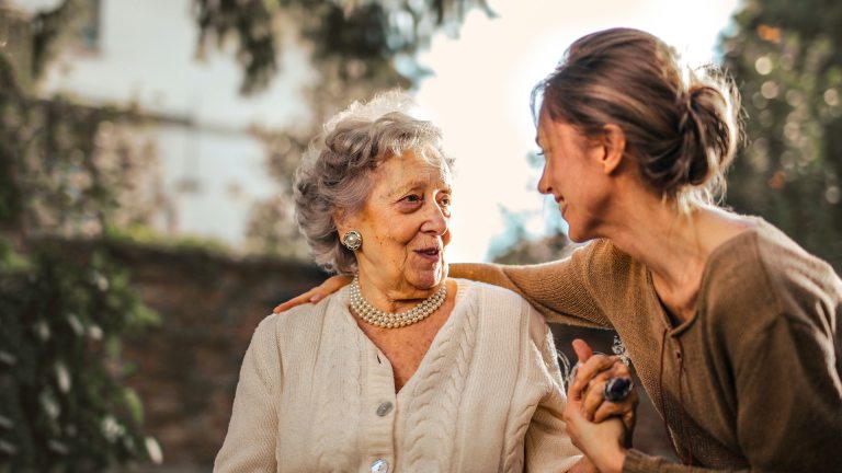 An elderly woman tlaks with a younger woman on a park bench