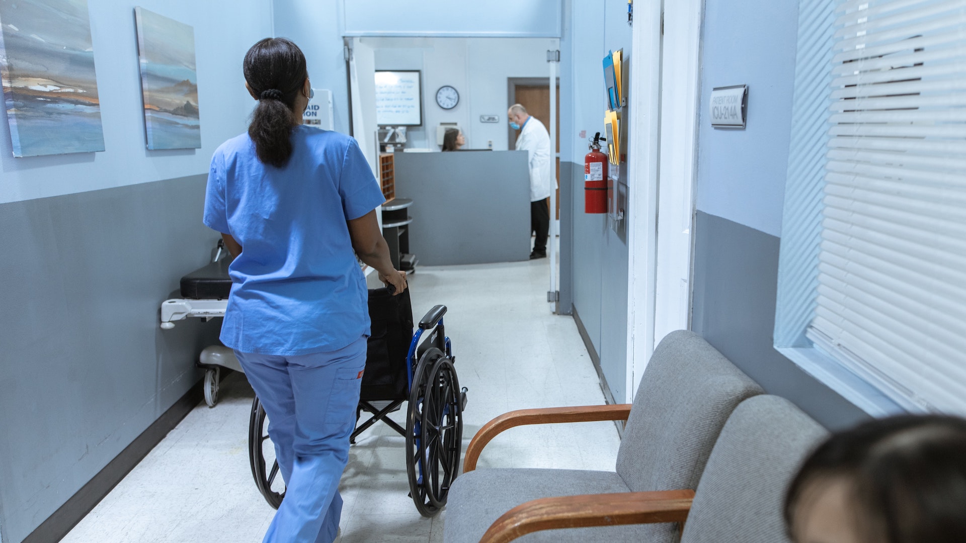 A nurse pushing an empty wheelchair down a hospital corridor, facing away from the corridor. Around 300,000 nurses did unpaid overtime during the pandemic.