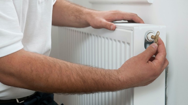 A man in a white shirt uses a radiator key