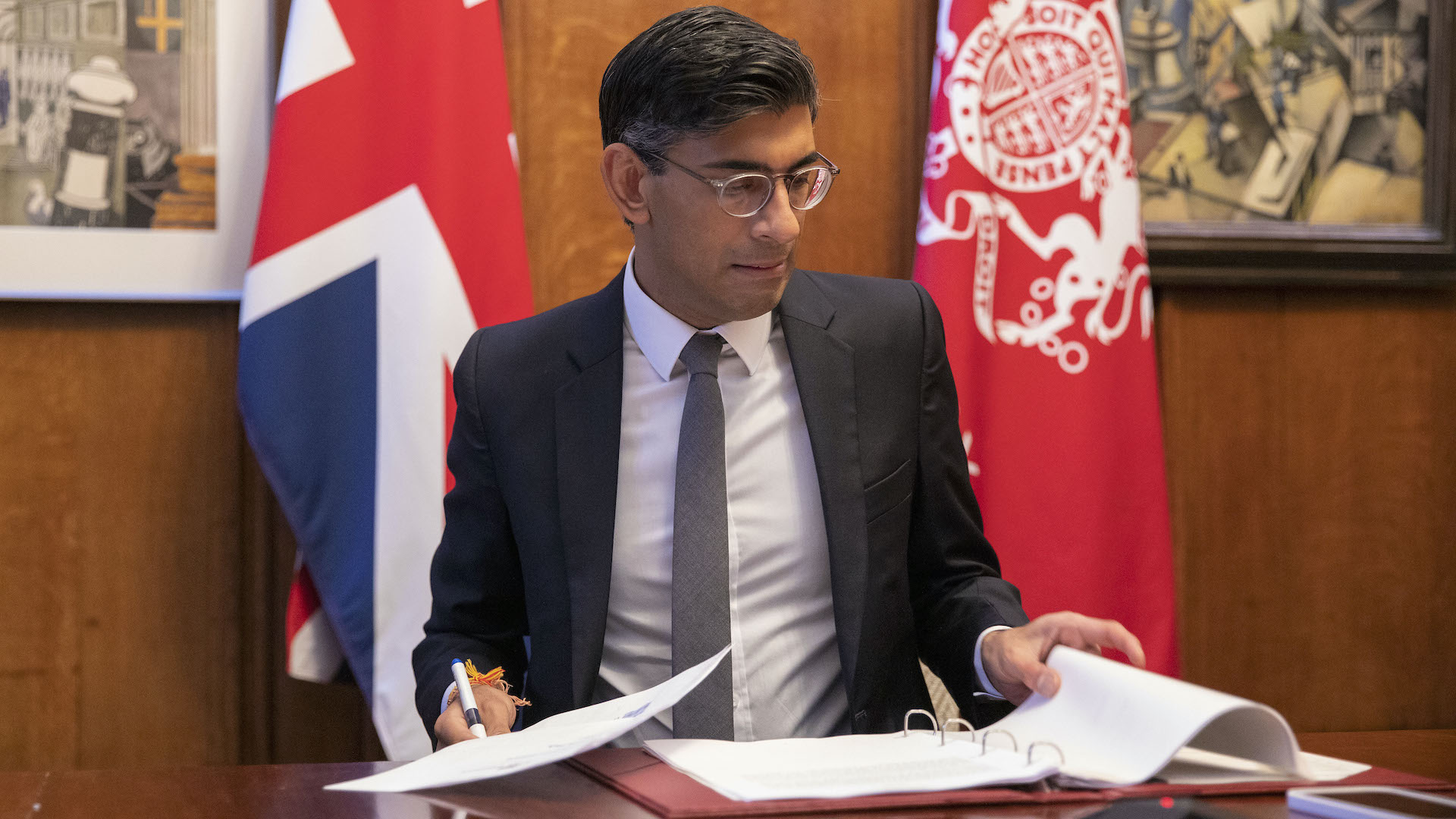 Rishi Sunak reviews paper at his desk in front of a union jack