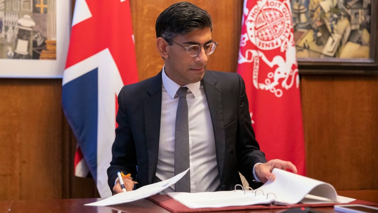 Rishi Sunak reviews paper at his desk in front of a union jack