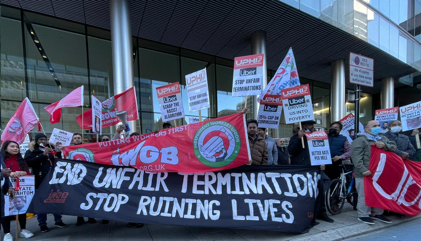 Uber drivers and members of Union IWGB protest outside Uber HQ in London holding a banner saying "end unfair terminations stop ruining lives."