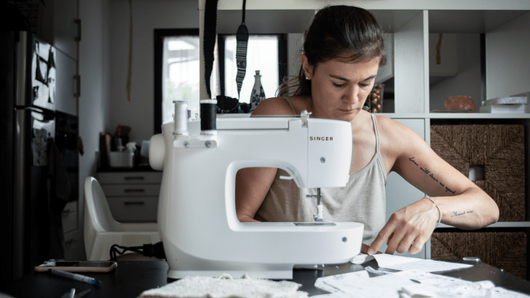 A woman uses a sewing machine sat at her kitchen table