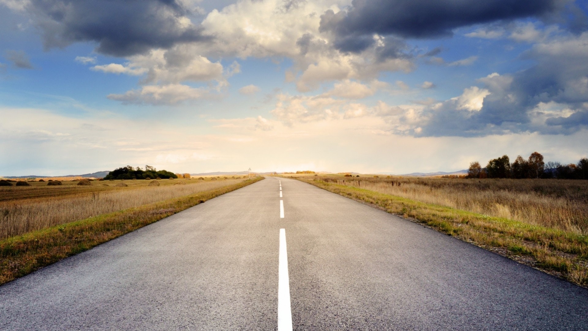 A road stretches out into the horizon and a clear, sunny sky