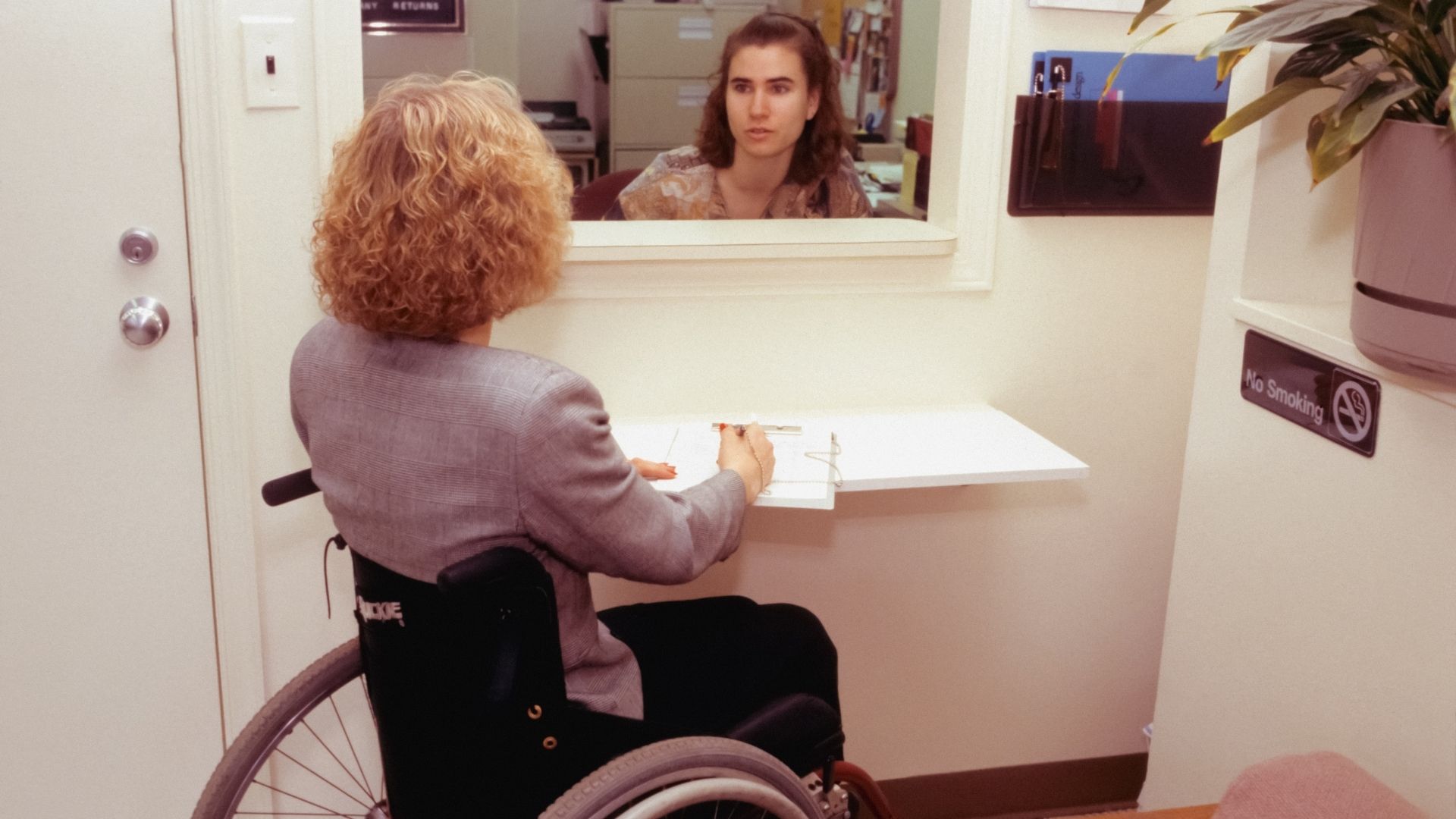 A woman in a wheelchair sits by a reception desk while talking to a
