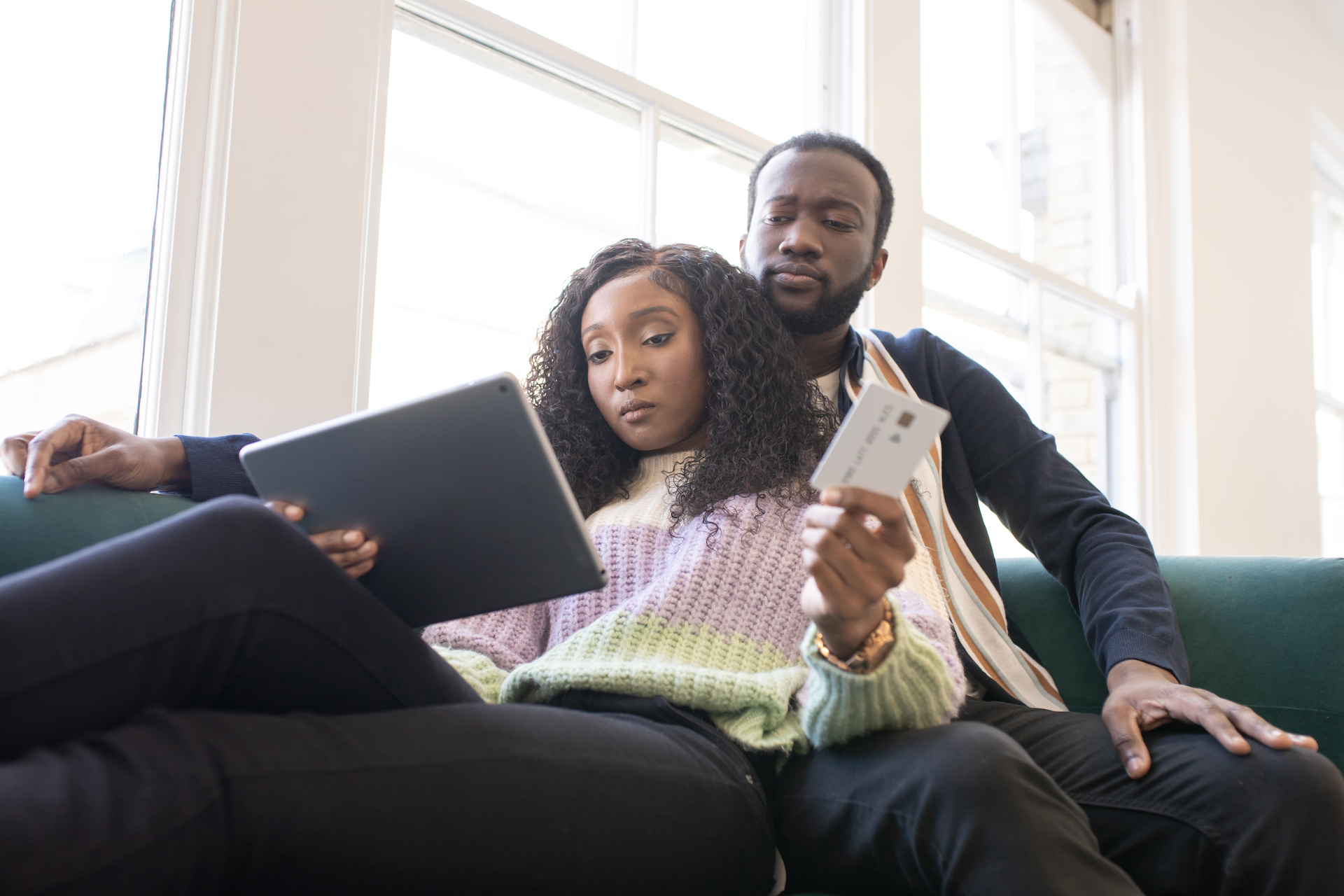 A young couple sit on a sofa with a credit card