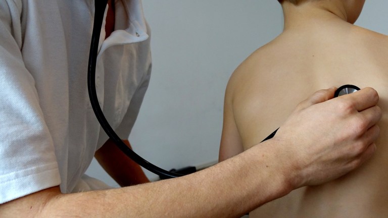 A doctor listening to a child's back through a stethoscope. Poverty