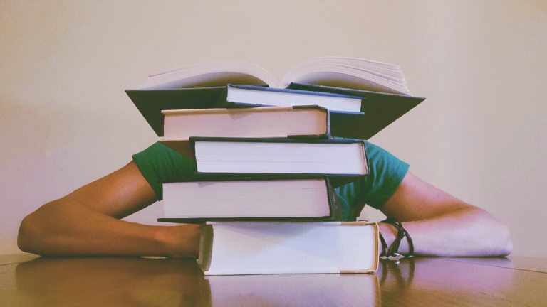 Someone sits behind a stack of books on a table