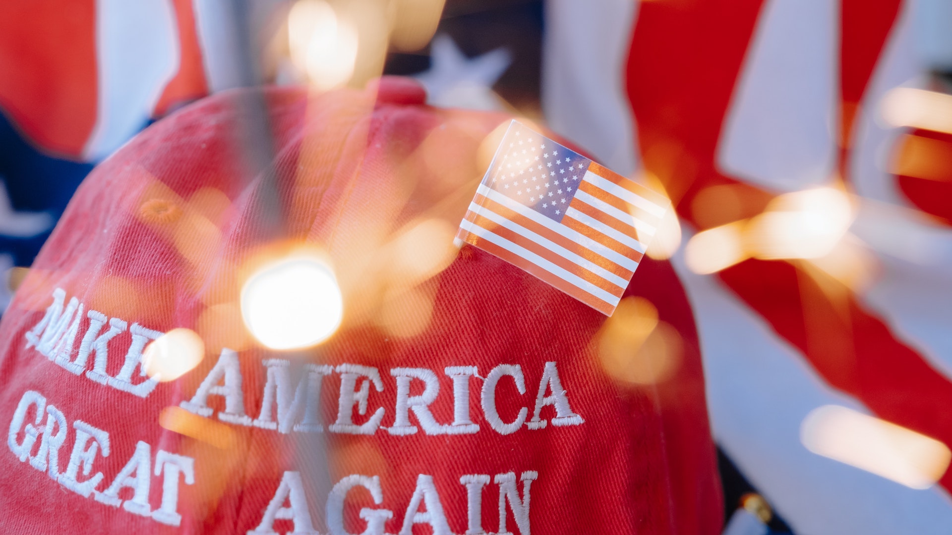 A 'Make America Great Again' hat, adorned with an American flag, with a sparkler in the foreground