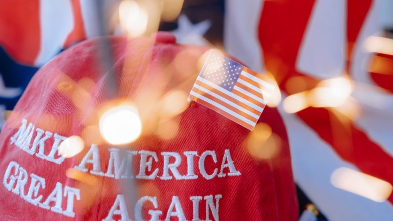 A 'Make America Great Again' hat, adorned with an American flag, with a sparkler in the foreground