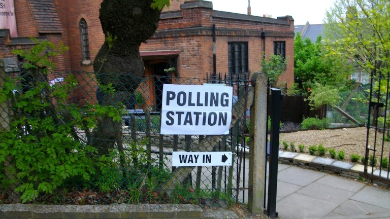 A polling station sign hangs on a wire fence outside a building
