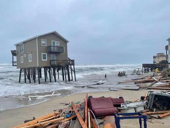 Image of house on stilts in water, surrounded by debris.