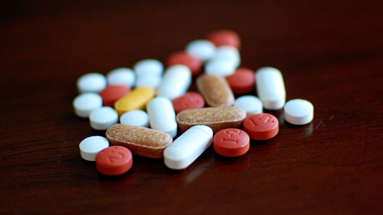 A handful of different colour pills sit on a dark wood table