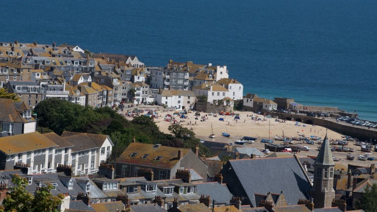 The rooftops and sandy beaches of St Ives in Cornwall are set against the blue background of the sea
