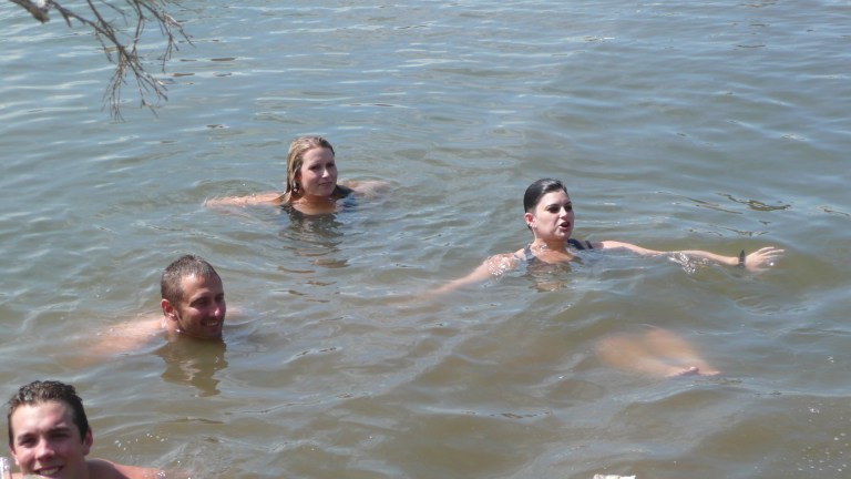 Four people swim in brown, murky river water