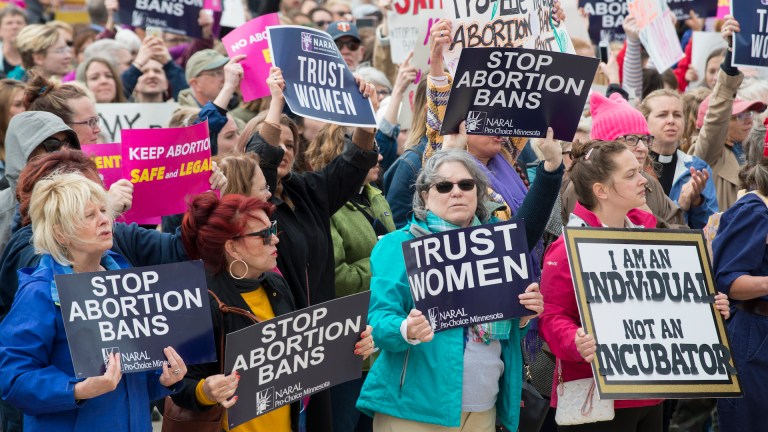Women hold signs saying