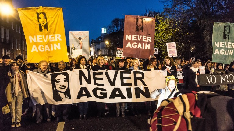 Women march holding banners and signs saying 