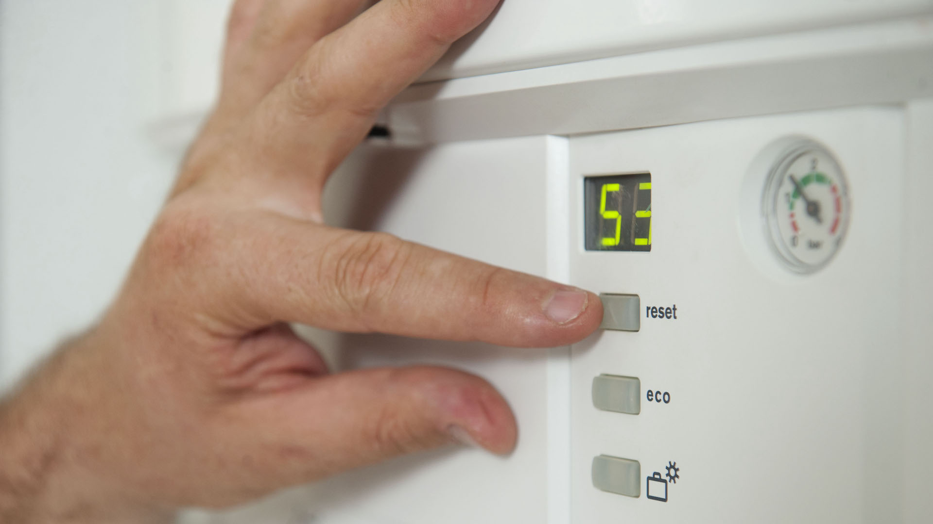 A hand points to buttons on a gas boiler