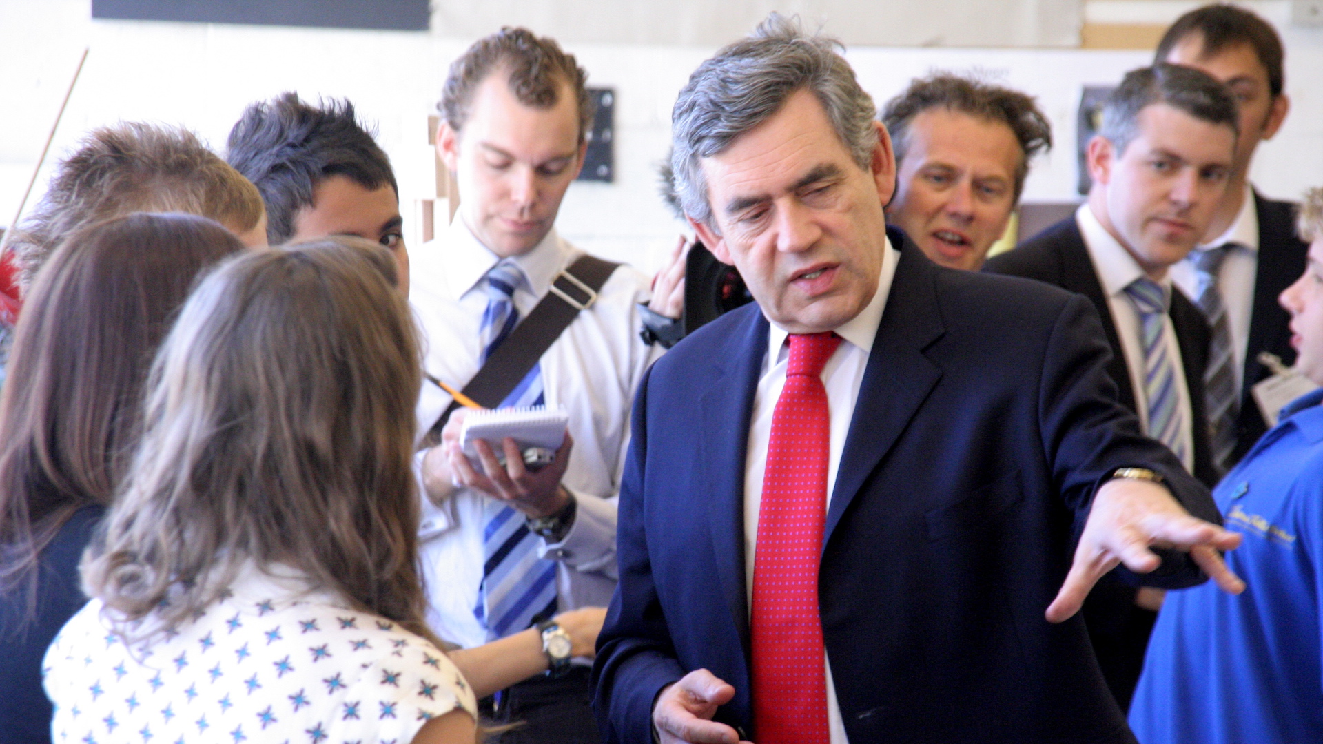 Gordon Brown wears a red tie and suit and talks to a woman with one hand outstretched