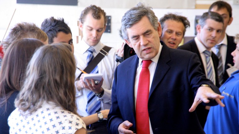 Gordon Brown wears a red tie and suit and talks to a woman with one hand outstretched