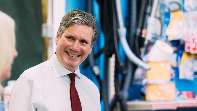 Keir Starmer wears a white shirt and red tie and smiles at the camera