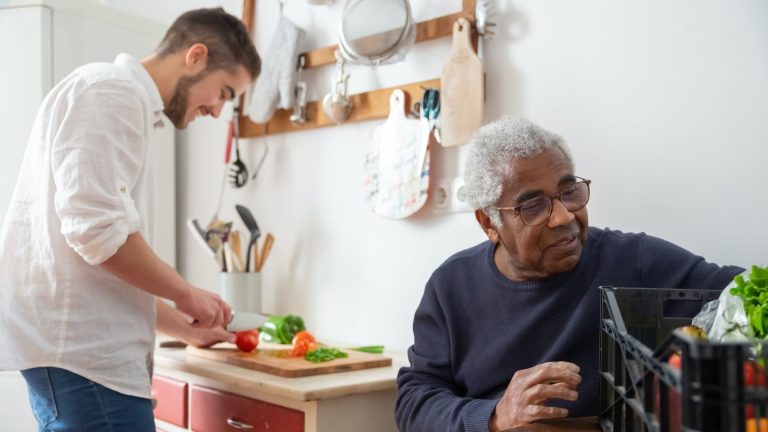 a man chops vegetables on a table behind an older man