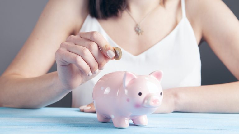 Woman putting money in piggy bank/ how make money