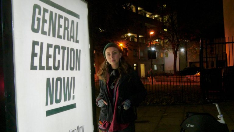 Journalist Eliza Pitkin stands next to General Election Now poster