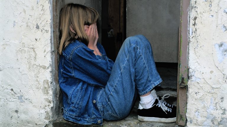 A young girls holds her head in her hands while sitting in a doorway