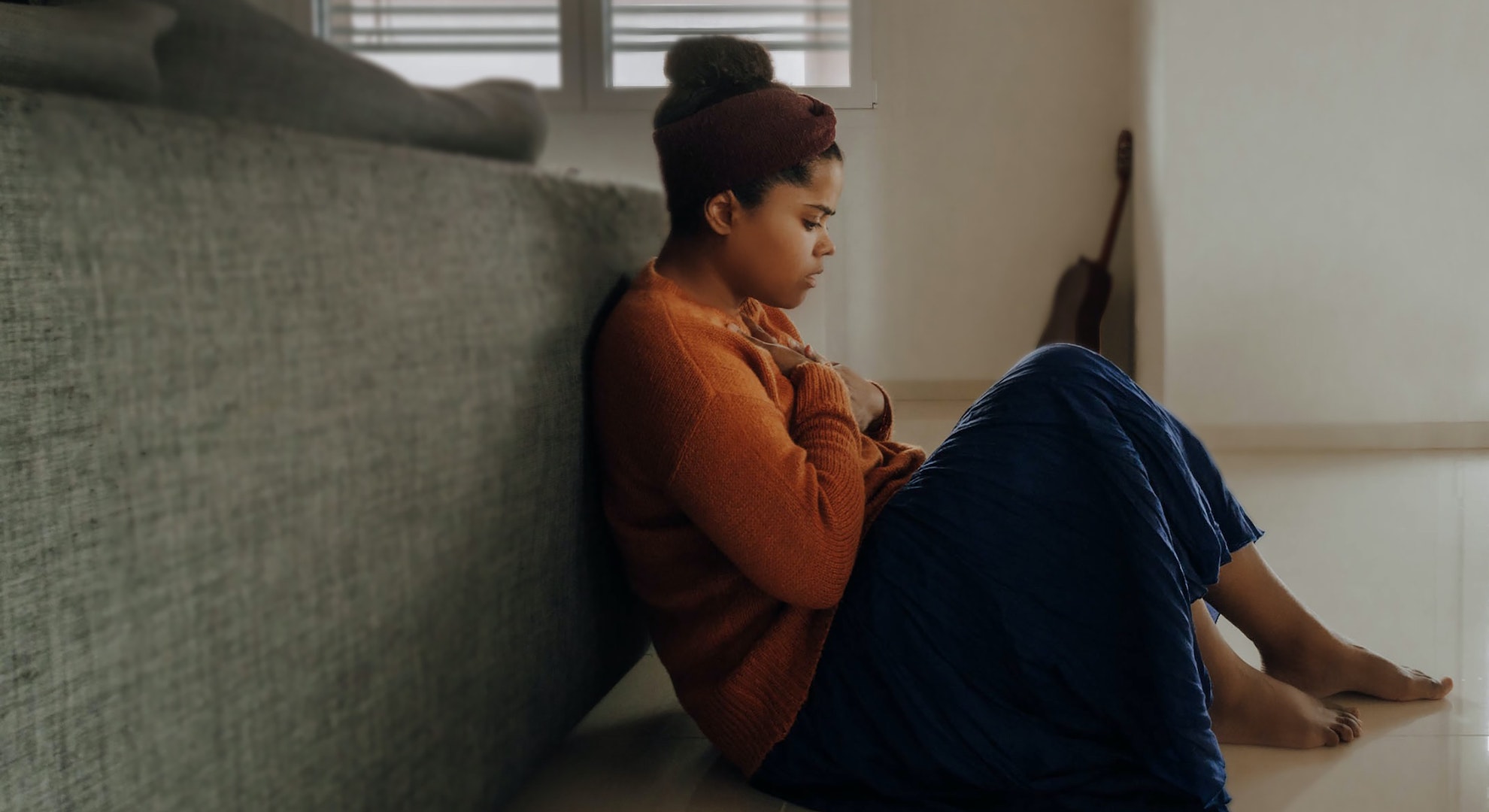 Woman sitting on the floor clutching her chest. 