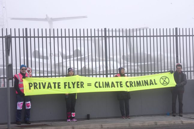Extinction Rebellion protesters stand at Luton Airport holding a sign reading 