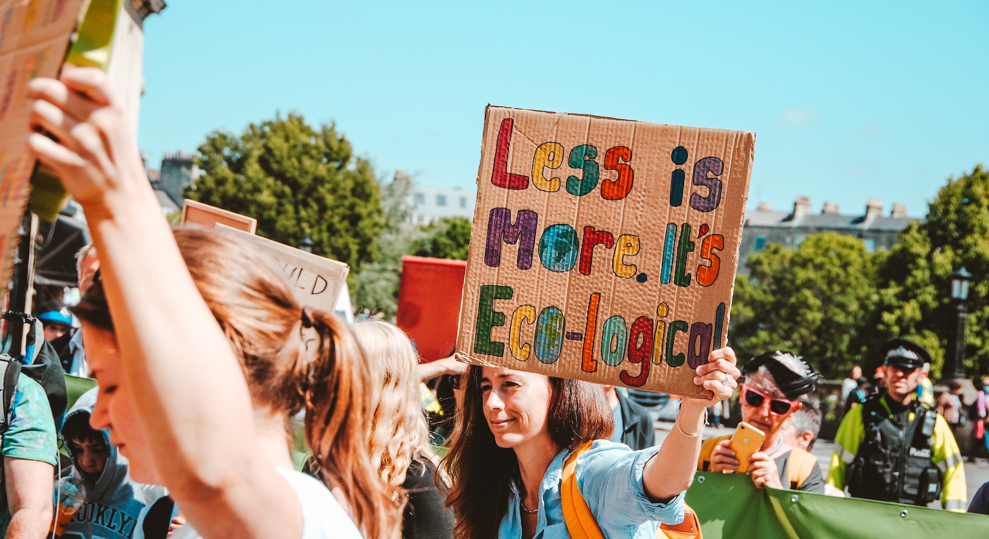 woman holding up sign at climate protest about overconsumption that says "less is more. It's Eco-logical"