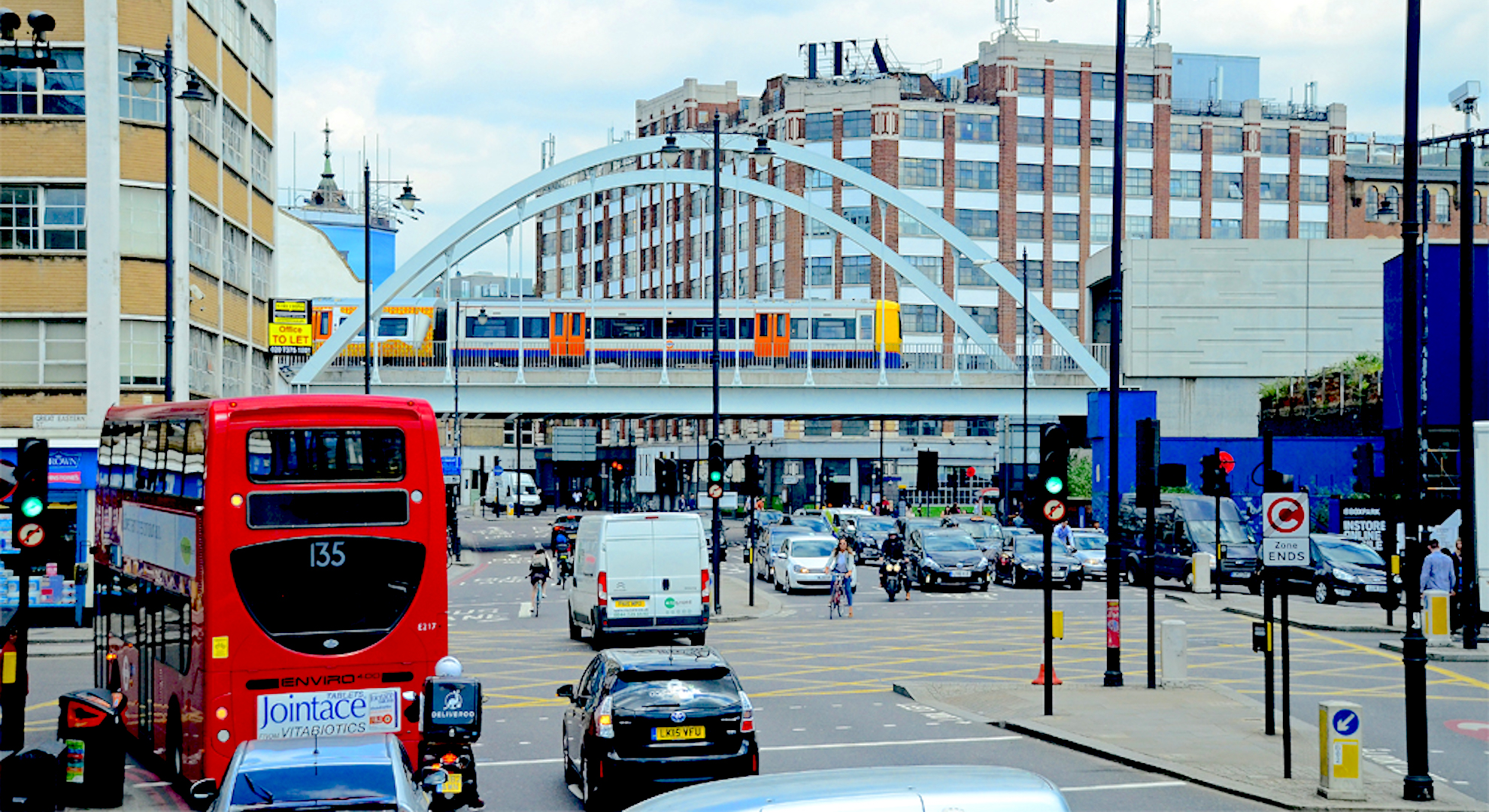 Vehicles including a red bus, white vans and black taxis wait at traffic lights in central London