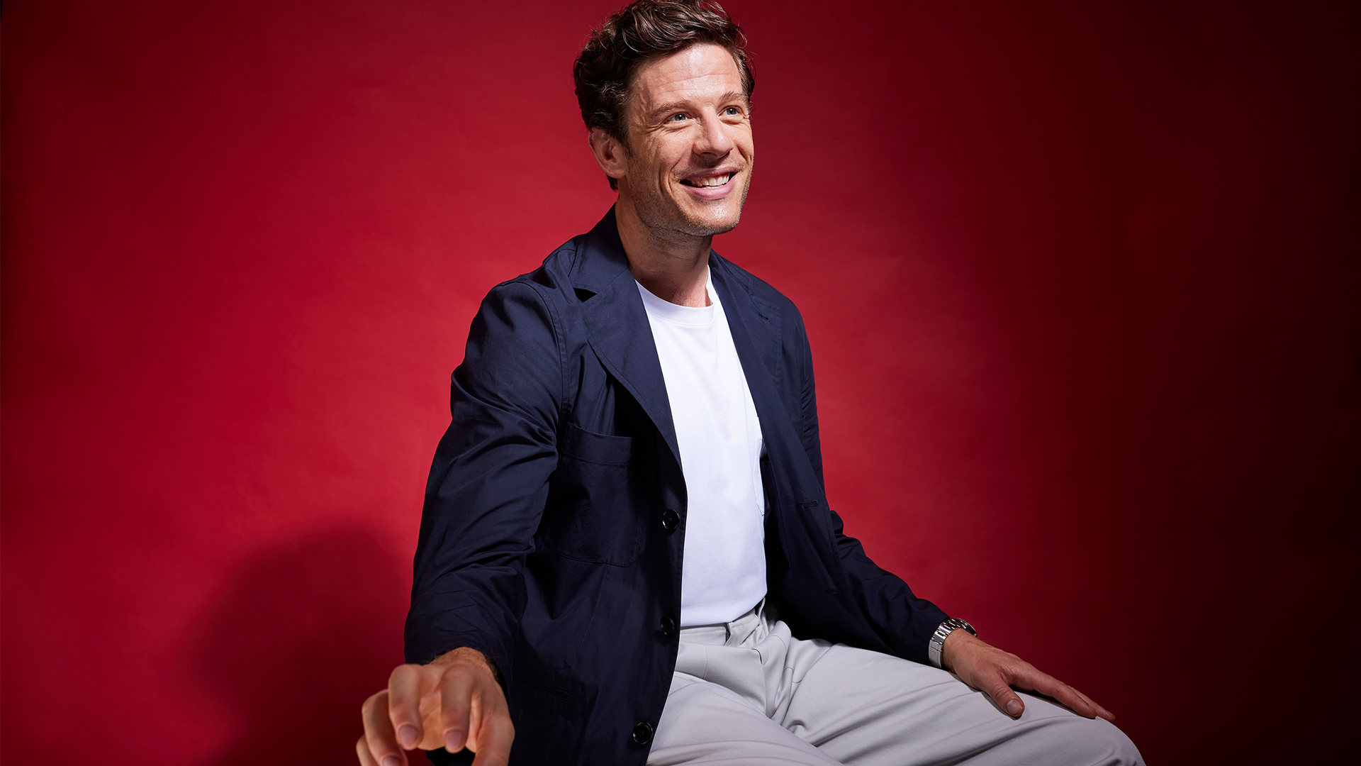 James Norton smiling, in a white t-shirt with a blue jacket