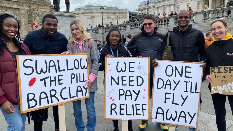 5 doctors stand in Trafalgar square holding placards such as 'we need pay relief'