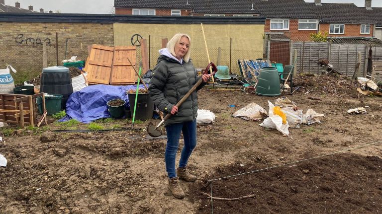 Carly Burd standing in her allotment holding a shovel and smiling